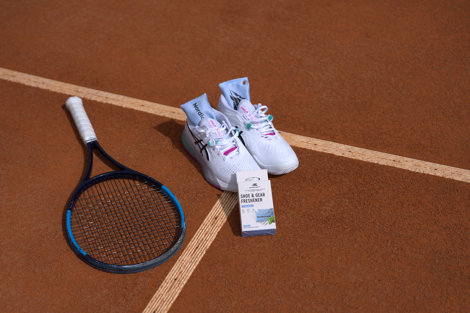NordicFresh Cool Mint bamboo charcoal shoe & gear freshener beside tennis shoes and racket on a clay court